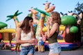 Two sisters, standing is front of attraction in theme park, holding popcorn in paper box, smiling, having fun. Pretty girls.