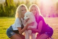 Two sisters twins beautiful curly blonde happy young women in denim shorts sitting at glass and hugging a white fluffy Royalty Free Stock Photo