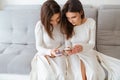 Two sisters twins sitting on couch and using mobile phones