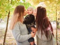 Two sisters of the twins, stand in an autumn park, kiss on both cheeks of a little boy, whom one of them is holding. Royalty Free Stock Photo