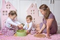 Two sisters sits on the floor in the kitchen with their mother and plays with dry pasta