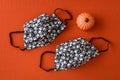 Two skull and bones, black and white fabric face masks, with a ceramic pumpkin, on an orange background