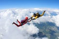 Two skydivers in color suits are falling above white clouds.