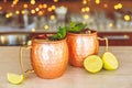 Two slylish Moscow mule cocktails in metallic cups with lemon and mint.