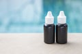 Two small black plastic bottle with white lit on swimming pool edge over blurred blue swimming pool Royalty Free Stock Photo