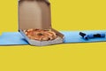 Two small blue dumbbells and a box with tasty pizza on a blue fitness or yoga mat. Isolated on a yellow background. Concept of Royalty Free Stock Photo