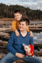 Two small boys sit in an embrace on logs by the river in the arms of a chihuahua dog Royalty Free Stock Photo
