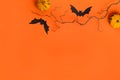 Two small decorative pumpkins, black paper bats, bare branch on bright orange background. Happy Halloween composition Royalty Free Stock Photo