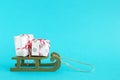 Two gift boxes wrapped of white and gray paper with red-white ribbon on a green wooden sleigh on a blue background. Royalty Free Stock Photo