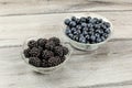 Two small glass bowls, one with blackberries, other blueberries, on gray wood desk Royalty Free Stock Photo