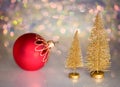 Two small gold Christmas tree and red christmas ball on a glass surface with defocused background with bokeh lights. Royalty Free Stock Photo