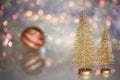 Two small Golden Christmas tree on the glass surface with defocused background with bokeh lights and a striped Christmas ball Royalty Free Stock Photo