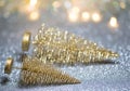 Two small Golden Christmas trees lie on a silver surface with defocused background with bokeh lights. Royalty Free Stock Photo