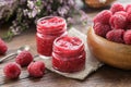 Two jars of raspberries jam, wooden bowl of fresh red raspberries on kitchen table