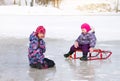 Two small kids have fun sitting together on the ice and playing with a snow sled on clear winter day Royalty Free Stock Photo
