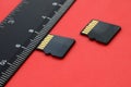 Two small micro SD memory cards lie on a red background next to a black ruler. A small and compact data and information store
