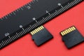 Two small micro SD memory cards lie on a red background next to a black ruler. A small and compact data and information store