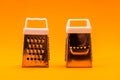 Two small shiny metal grater isolated on orange background, close-up of cheese and food stainless grater. Horizontal orientation