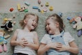 Two small sisters playing with different toys at home, lying on the floor Royalty Free Stock Photo