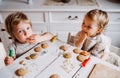 Two small toddler children sitting at the table, decorating and eating cakes at home.