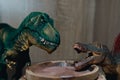 Two small toy dinosaurs over a wooden bowl of food on the shelf Royalty Free Stock Photo