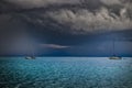 Two small yachts in sea with storm weather near Cagliari, Italy. In the distance it rains a lot and lightning falls. The clouds Royalty Free Stock Photo