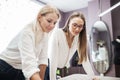 Two smart-looking pretty women wearing white shirts are leaning over the sewing table. Fashion, tailor`s workshop. Royalty Free Stock Photo