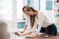 Two smart-looking pretty women wearing white shirts are leaning over the sewing table. Fashion, tailor`s workshop. Royalty Free Stock Photo