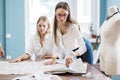 Two smart-looking pretty women wearing white shirts are pointing at the sewing cutting-out. Fashion, tailor`s workshop. Royalty Free Stock Photo