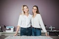 Two smart-looking pretty women wearing white shirts are standing over the sewing table. Fashion, tailor`s workshop. Royalty Free Stock Photo