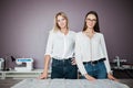 Two smart-looking pretty women wearing white shirts are standing over the sewing table. Fashion, tailor`s workshop. Royalty Free Stock Photo