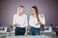 Two smart-looking pretty women wearing white shirts are talking over the sewing table. Fashion, tailor`s workshop. Royalty Free Stock Photo