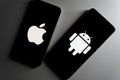 Two smartphones at an angle displaying Apple and Android logos on black screens. Royalty Free Stock Photo