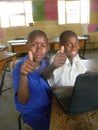 Two African school children with laptop showing thumbs-up