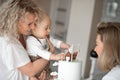 Two smiling beauteous middle-aged and young women congratulate cute little one-year-old boy touching bear on white cake. Royalty Free Stock Photo