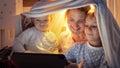 Two smiling boys in pajamas playing video games on tablet computer with mother at night. Family having time together, parenting, Royalty Free Stock Photo