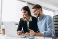 Two smiling businesspeople sitting together at a table in a modern office talking and using a laptop Royalty Free Stock Photo