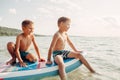 Two smiling Caucasian boys kids sitting on paddle sup surfboard in water. Children friends talking laughing. Modern outdoor summer Royalty Free Stock Photo