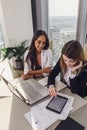 Two smiling female colleagues working together in office sitting at desk using laptop and tablet pc Royalty Free Stock Photo