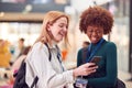 Two Smiling Female College Student Friends Checking Mobile Phone In Busy Communal Campus Building Royalty Free Stock Photo