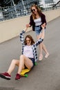 Two smiling female friends having fun riding yellow longboard on the street. Friendship concept Royalty Free Stock Photo