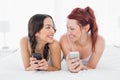 Two smiling female friends text messaging on bed Royalty Free Stock Photo