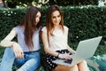 Two smiling female students are sitting on the grass in the street. They are working on laptop at campus. Royalty Free Stock Photo