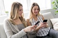 Two smiling girl friends in casual wear work in telephones sitting on the sofa at home. Royalty Free Stock Photo