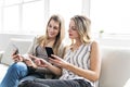 Two smiling girl friends in casual wear work in telephones sitting on the sofa at home. Royalty Free Stock Photo