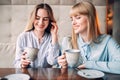 Two smiling girlfriends drinks coffee in cafe