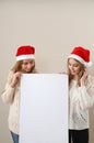 Two smiling girls in Santa`s red hat looking at big white empty card. Happy holiday concept Royalty Free Stock Photo
