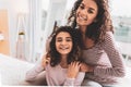 Two smiling girls sitting in armchair near decorative plants