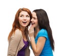 Two smiling girls whispering gossip