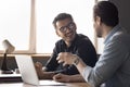 Two millennial businessmen having discussion seated at desk with laptop